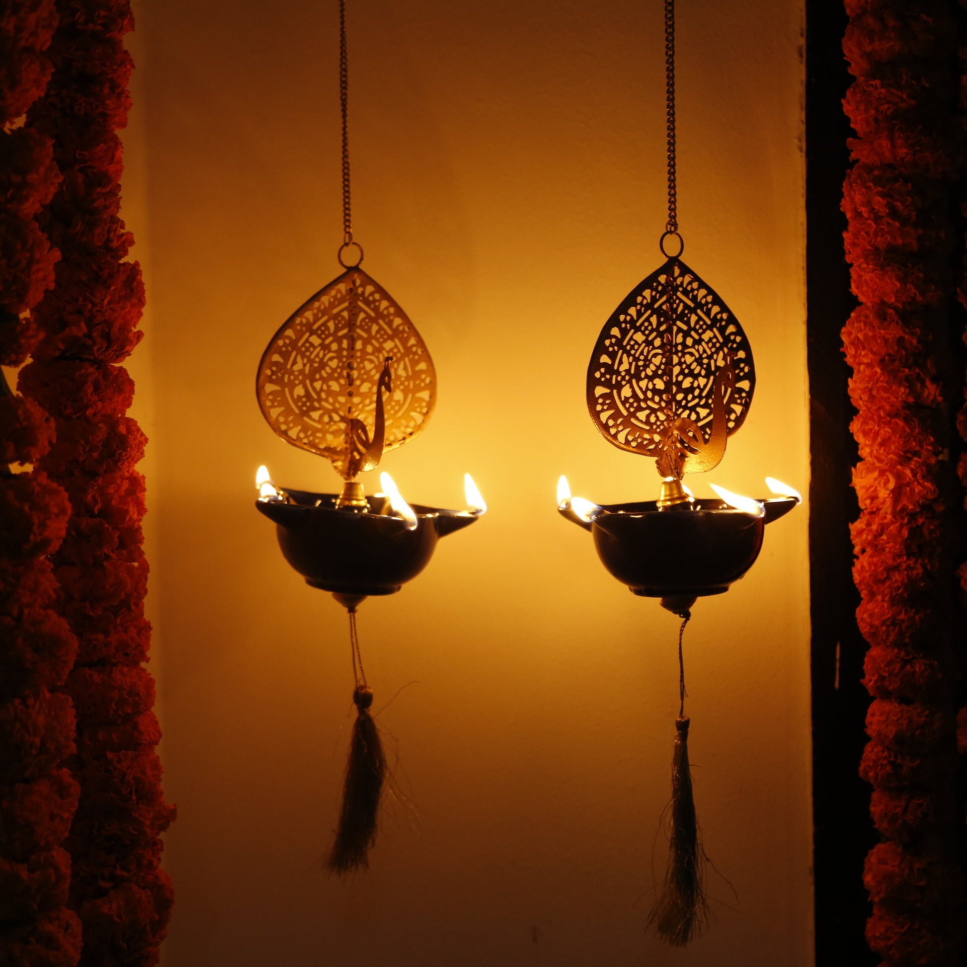 Decorative Peacock Swagata long chain T-light holder oil lamps with floral garlands on a warm-toned background