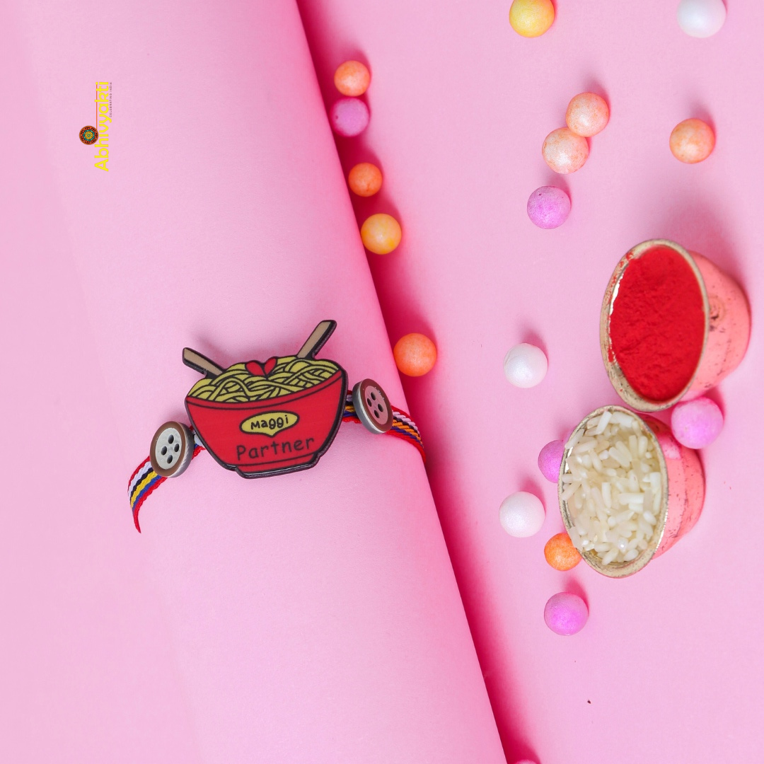 Quirky Rakhi featuring a red bowl of noodles with “Maggi Partner” text, paired with multicolored thread and cute button accents — perfect for celebrating sibling bonds with a fun, foodie twist.