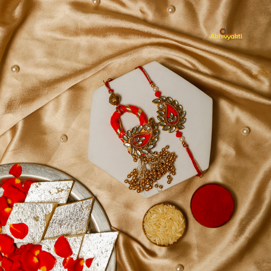 A red and gold rakhi lumba adorned with intricate paisley designs and a shimmering gold and red thread, symbolizing sibling, Bhaiya bhabhi love and protection