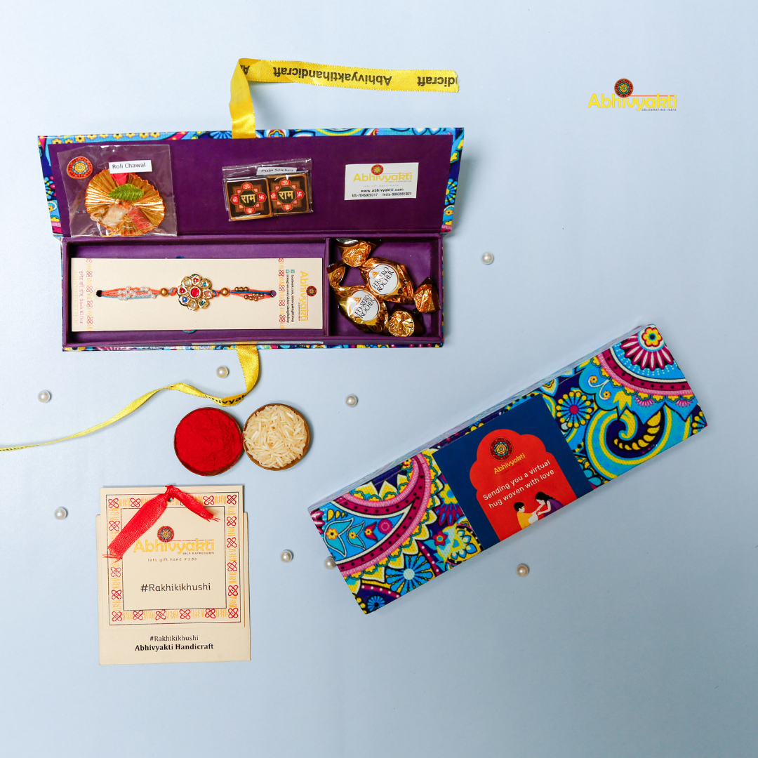 Traditional Rakhi with a round, floral gold centerpiece decorated with multicolored stones and pearls, on orange and blue threads, displayed on a light blue background