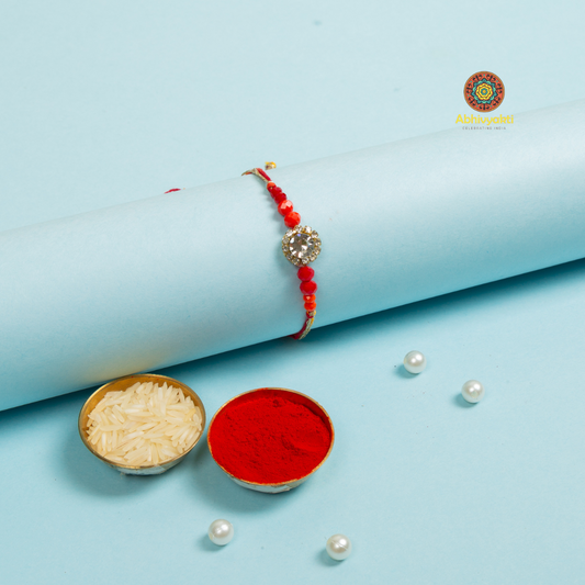 Rakhi bracelet featuring, pearls, stone, and red beads in a decorative design.