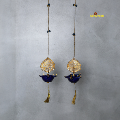 Two hanging decorative peacock swagata diya with gold and blue designs on a gray background