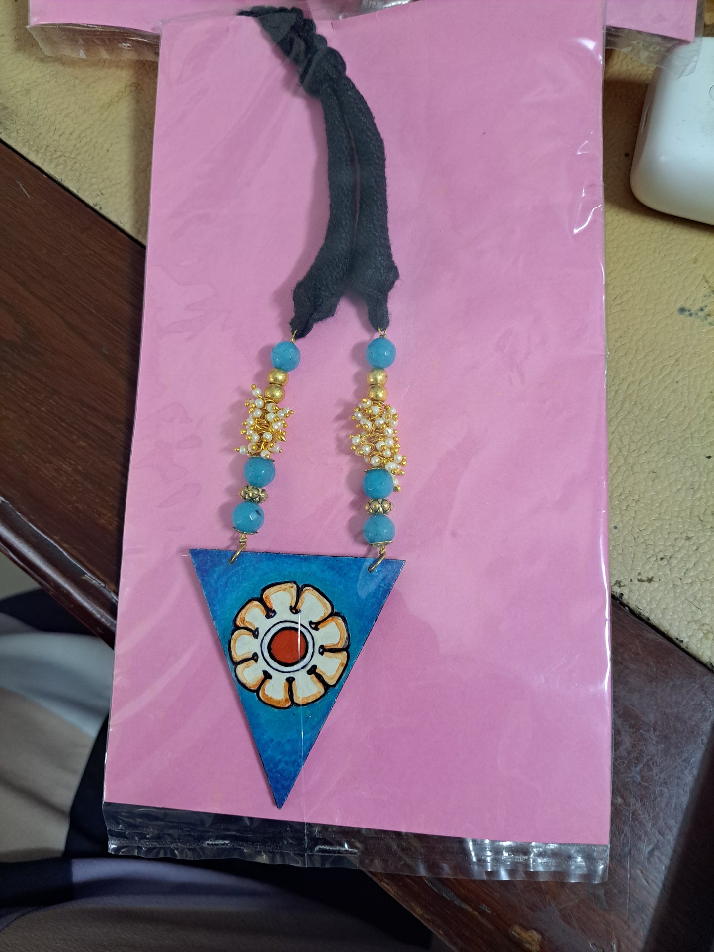 This beautiful Blue Triangle Adjustable Necklace with Wooden Pendant is hand painted and an exquisite Indian Jewellery inspired by Kerala Mural Art designed on crafted wood. It is surely an elegant wear for any occasion. A perfect head turner and a conversation starter..