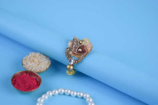Elegant gold and silver ring featuring pearl and bead, accompanied by zari rakhi with beads and stone.