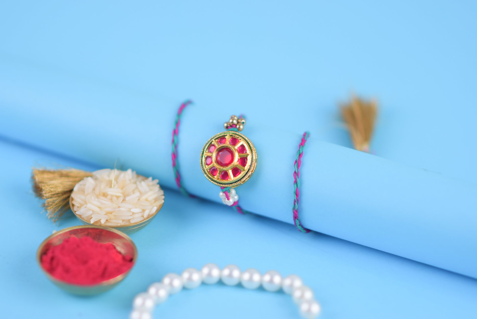 Rakhi bracelet featuring a flower, pearls, and red stone against a blue backdrop.