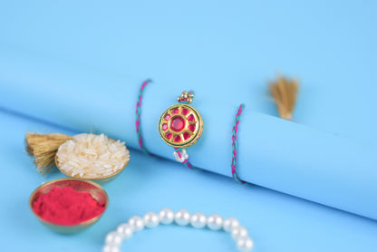 Rakhi bracelet featuring a flower, pearls, and red stone against a blue backdrop.