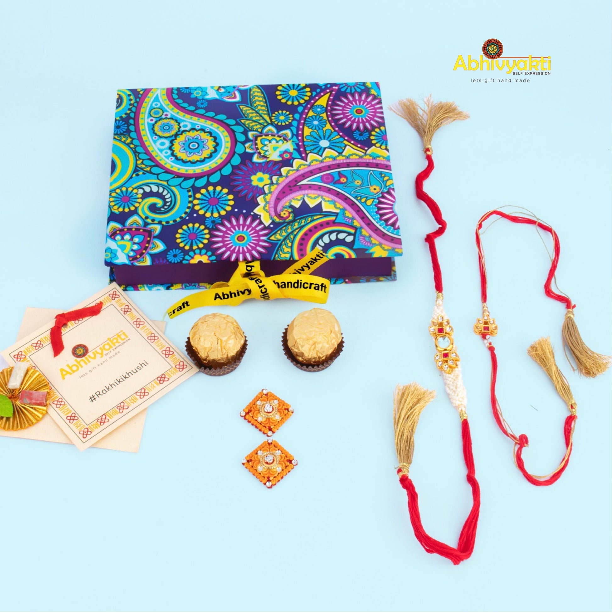 Elegant lumba rakhi set with red threads, golden tassels, and intricate kundan designs, displayed on a maroon background with chocolates and pooja soan.