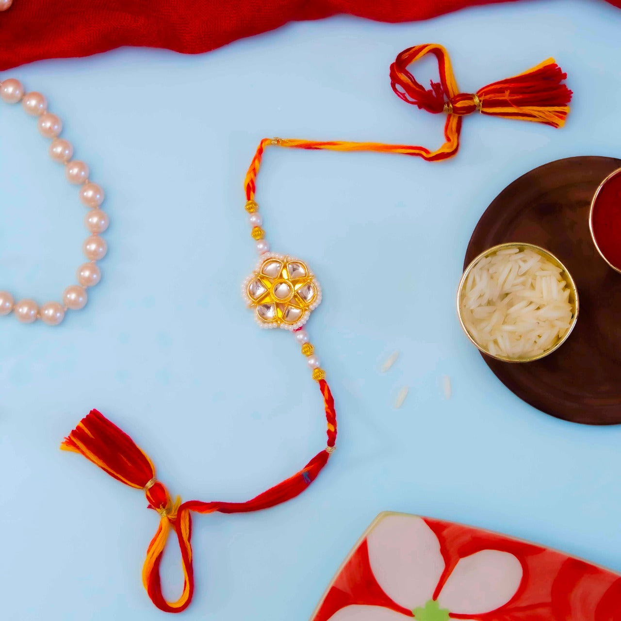 Red and gold kundan rakhi with pearls and beads, embellished with stones and beads.