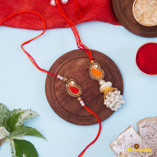 Red and white rakhi, each showcasing a special paisley lumba design with intricate stone and bead decorations, arranged on a plate.