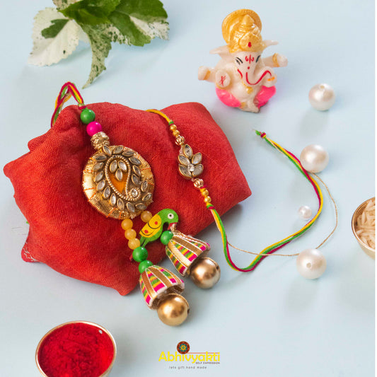 A gold rakhi with a pearl and pearl bead, featuring a unique design with stone and beads.
