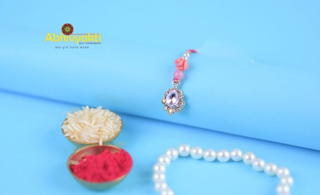 Elegant pink rakhi adorned with pearls and a single pearl, featuring stone and bead details.